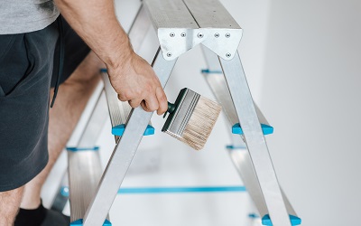 A person standing on a ladder, paintbrush in hand