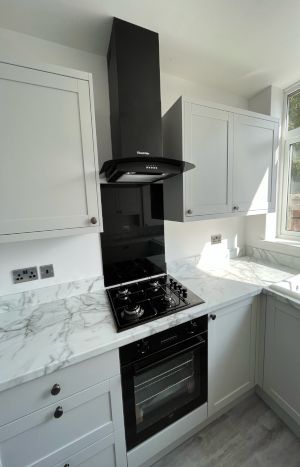 A corner of a light kitchen, showing white worktops and cabinets with a black oven and hob.